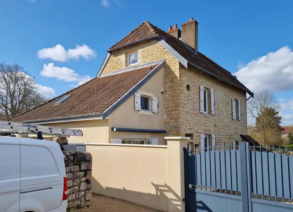 Un ouvrier en vêtements sombres et gants orange installe un bardage bois vertical sur la façade extérieure d'une maison moderne
