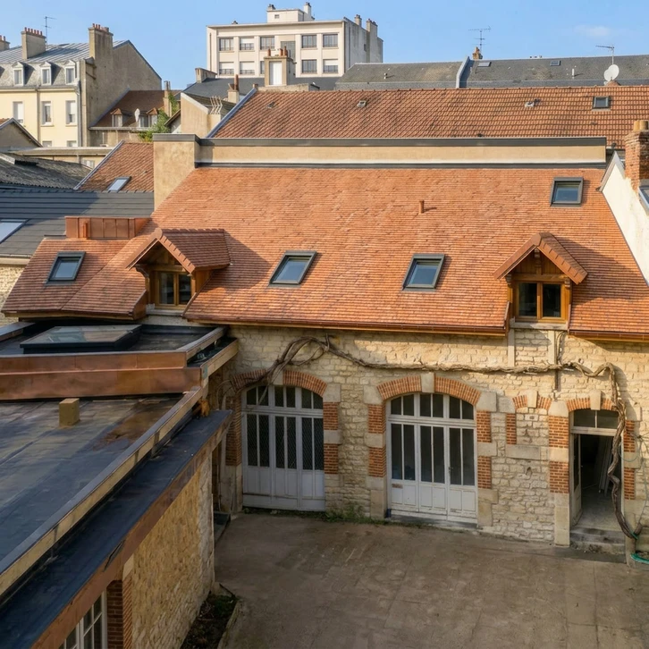 Un ouvrier en vêtements sombres et gants orange installe un bardage bois vertical sur la façade extérieure d'une maison moderne